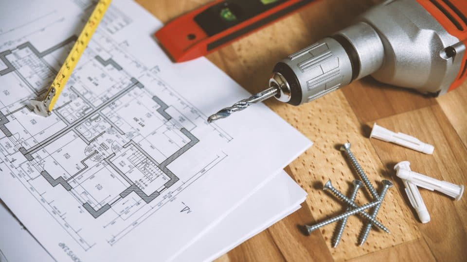 House floor plans with a tape measure, level, drill and screws on a wooden table