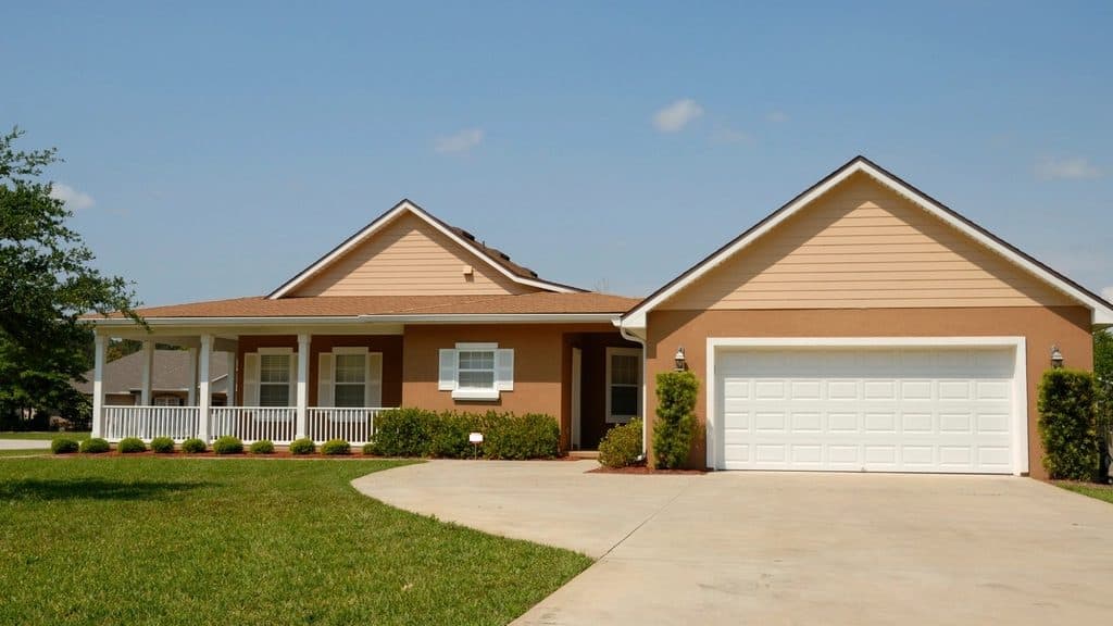 Single-story house with a front porch and a white double garage door at the end of a curved driveway