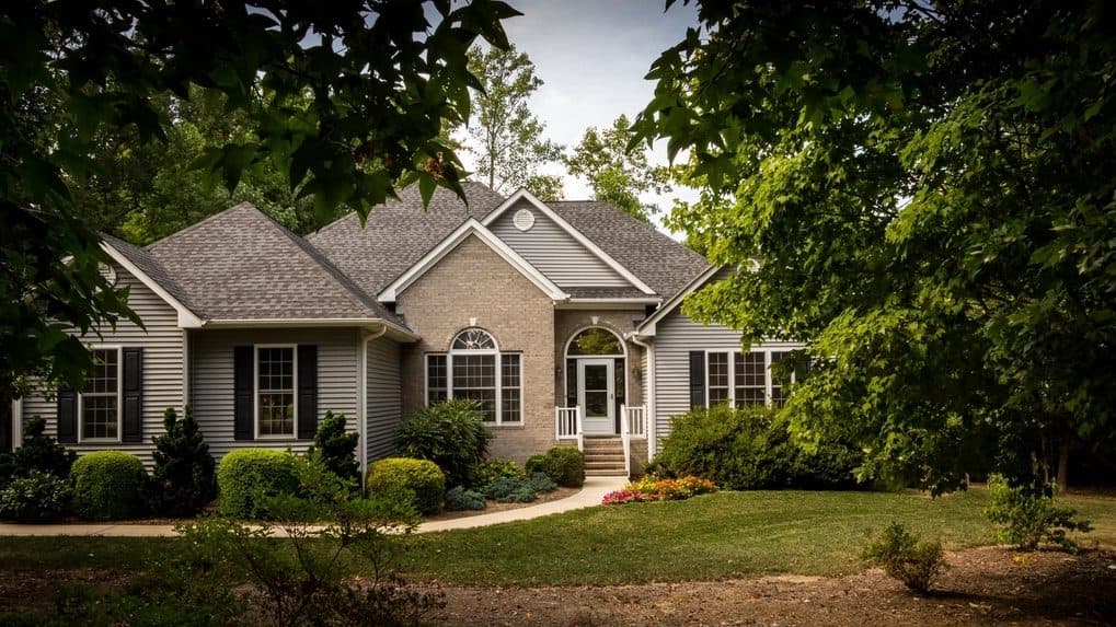 Single-story brick and siding house with shrubs, framed by shade trees