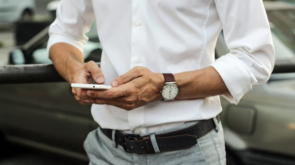 Man in a white shirt using a smartphone, shown from the shoulders down